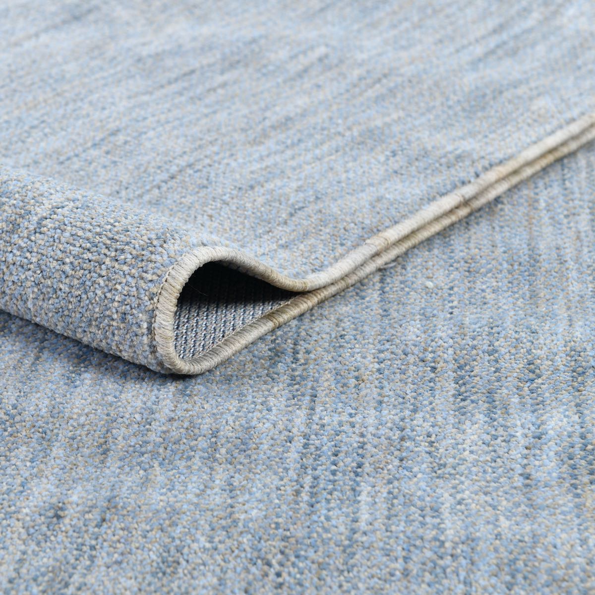 COD-17 Well Woven Moor Washable Rug: close-up of the soft blue rug, slightly rolled to showcase it's eco-friendly, stain-resistant pile
