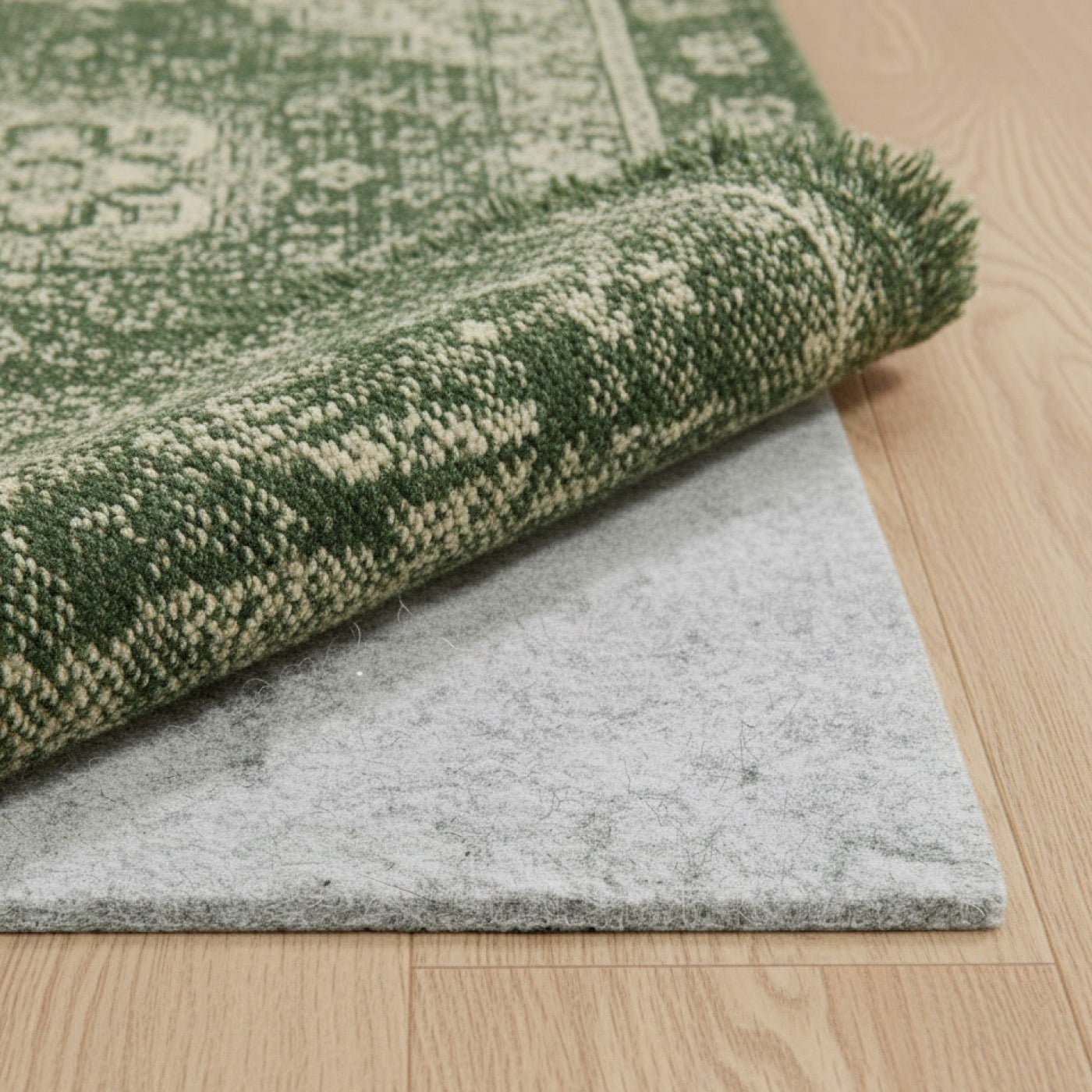 Green patterned rug on a wooden floor with gray custom size felt rug pad underlay