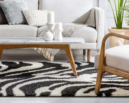 Safari Zebra Black Contemporary Shag Rug - Well Woven - The zebra rug styled under a neutral sofa with a coffee table and plant, offering a cozy, contemporary look.