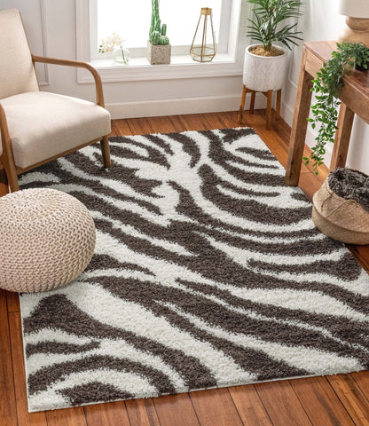 Safari Zebra Brown Contemporary Shag Rug - Well Woven - A bold brown and white zebra-print rug placed under a curved accent chair on hardwood floors with cozy, neutral decor.