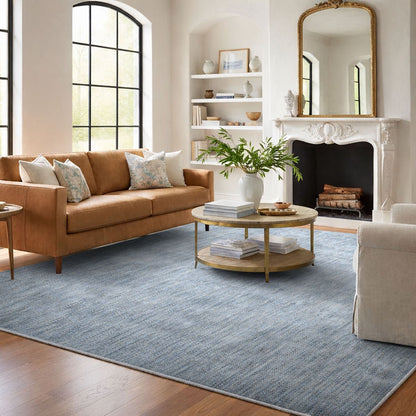 COD-12 Well Woven Moor Washable Rug - Living room with brown sofa, coffee table, and fireplace. A misty blue washable rug made of recycled polyester anchors the room.
