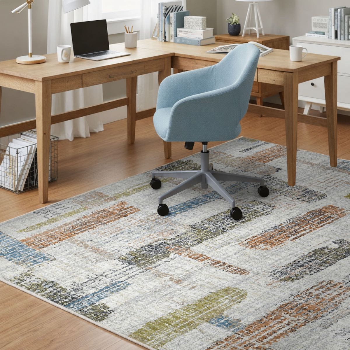 COD-51 Well Woven Fen Washable Rug - Home office with wooden L-shaped desk, blue chair, and a low pile abstract office rug in shades of grey, cream, green, blue and orange