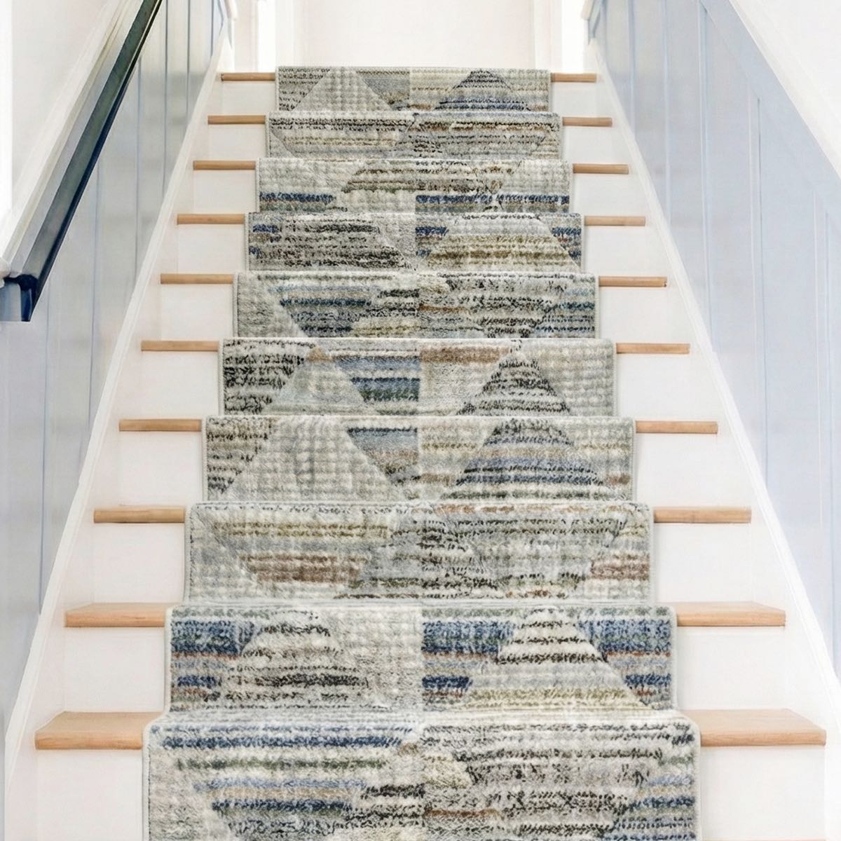 ELM-11-R - Staircase with a soft geometric runner rug in grey, blue and cream on wooden steps with white risers. Light blue board and batten lines the walls.