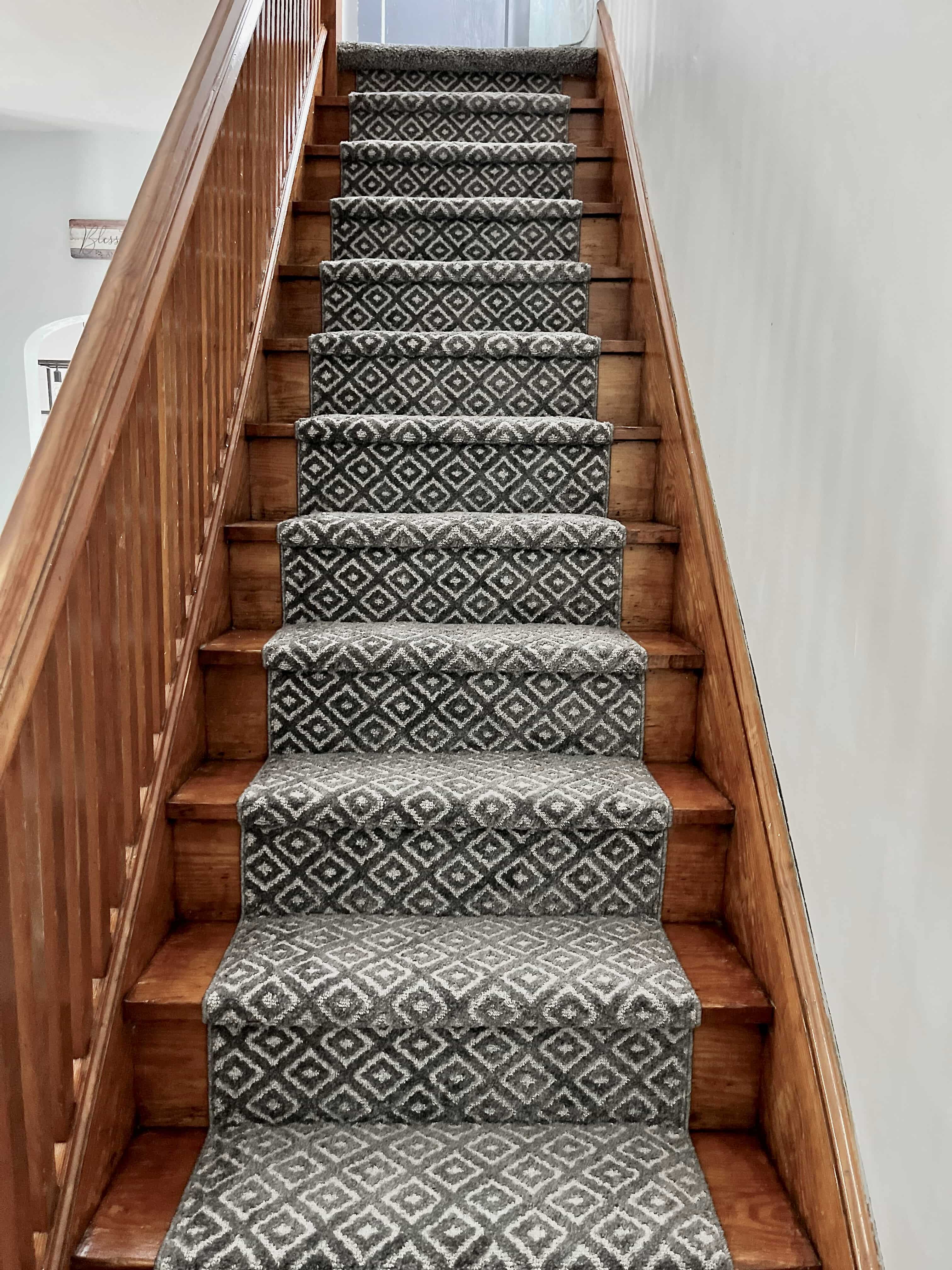 Staircase with patterned gray and ivory geometric carpet running up wooden steps.