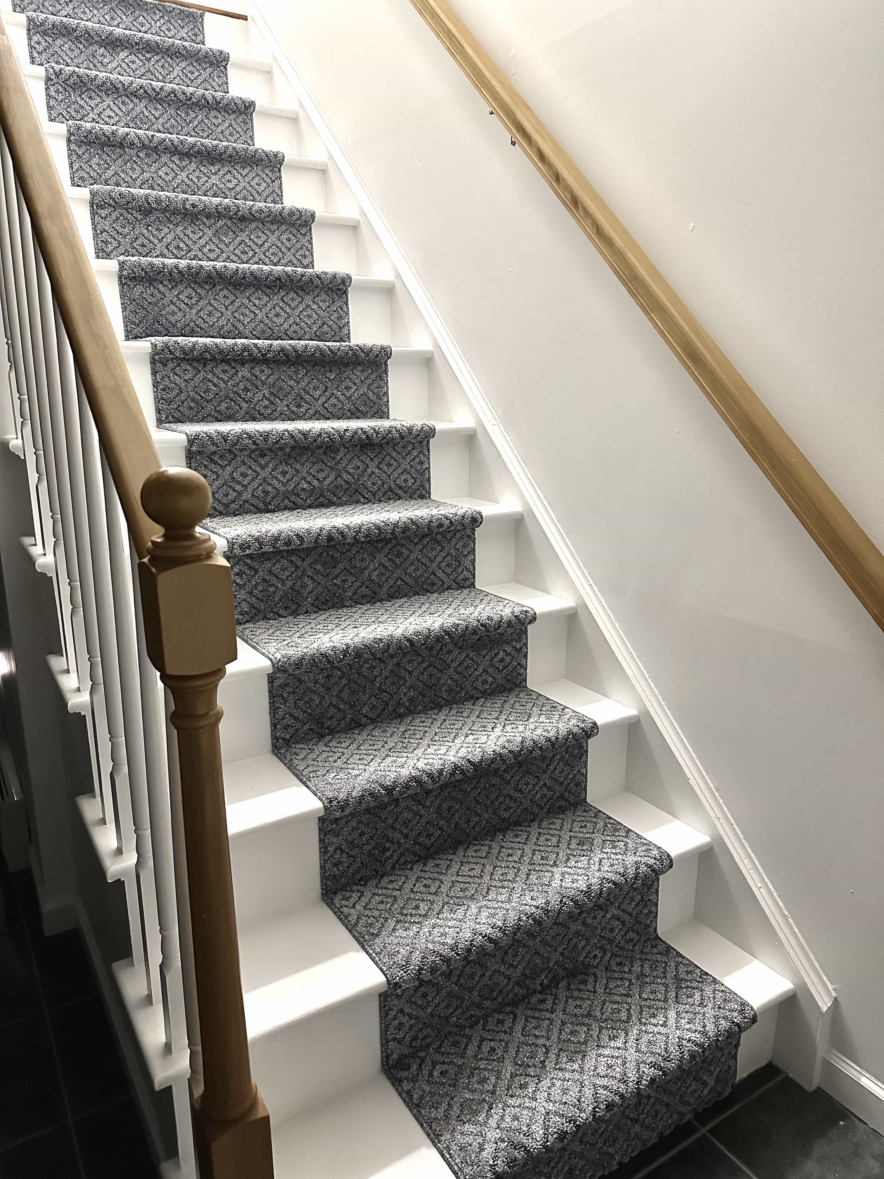 Staircase with patterned gray carpet and wooden banister.