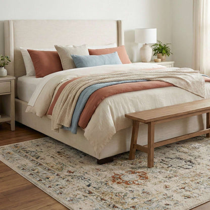 OM-122 – Bedroom with a beige upholstered bed and a cream vintage distressed rug with rust and gray accents on wood flooring.