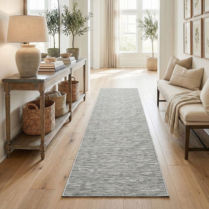 The Apollo Striations, a long,  gray well woven custom size runner, in a hallway with a wooden console table, and beige sofa