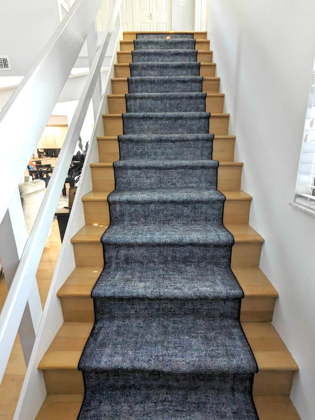 Staircase with a long blue rug on the steps and wooden risers in a well-lit room.