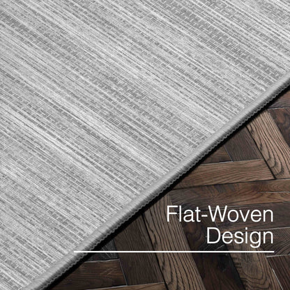 Edwin Custom Rug - Monochrome Striation , Flat Pile, Easy  Clean, Customizable for Your Space - Well Woven - Angled close-up of the light grey rug with text: “Flat-Woven Design.”