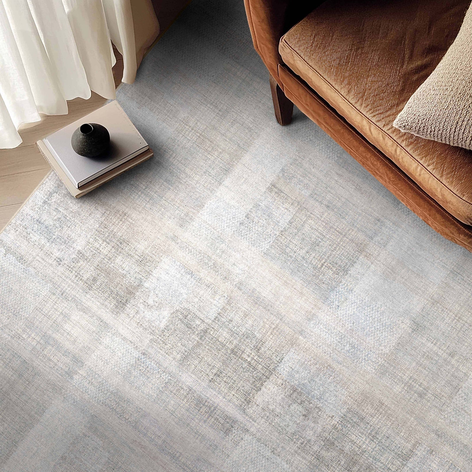 Gray textured custom rug in a living room setting with a brown sofa and white curtains.
