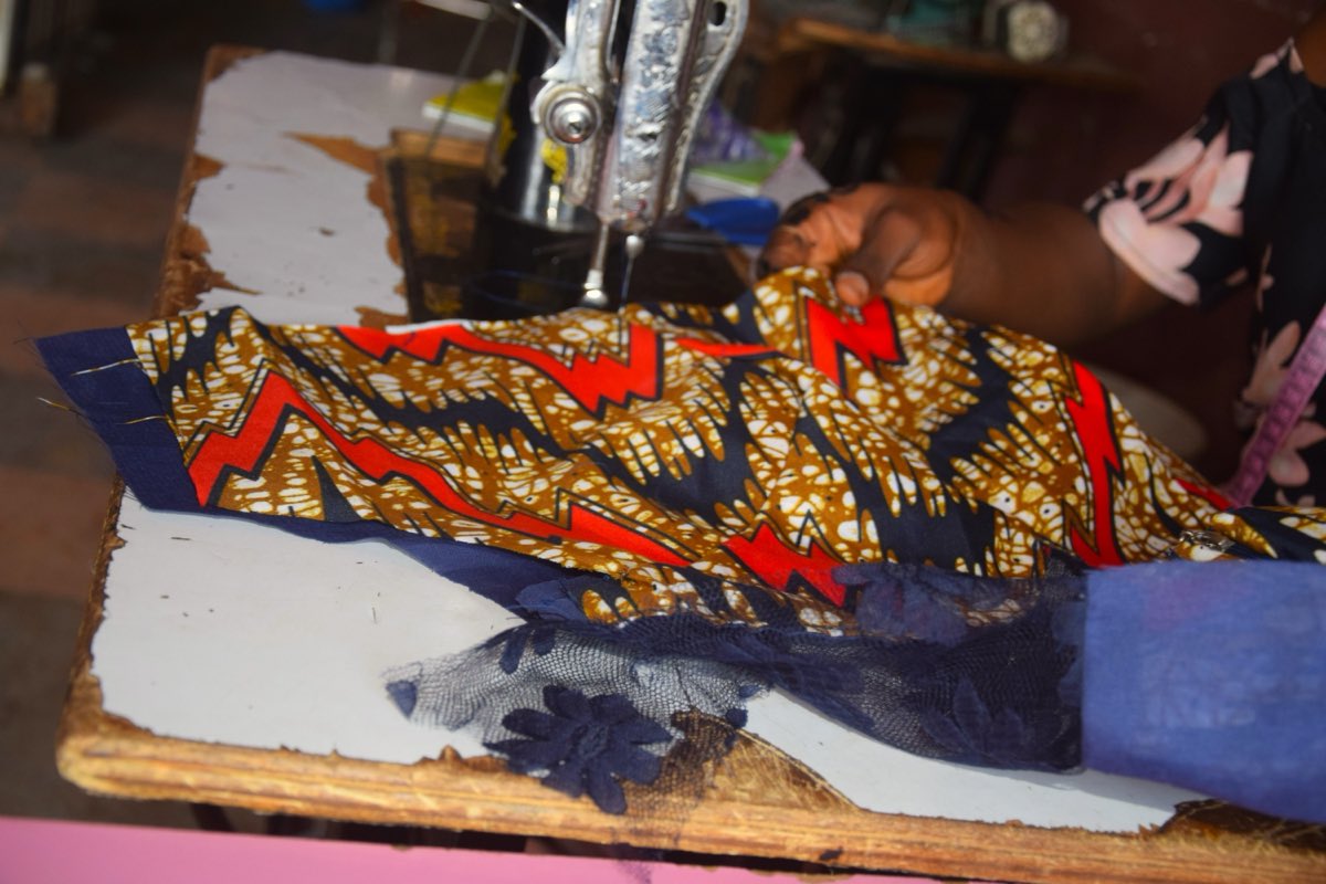 A tailor's hands guiding bold Ankara wax-print cloth through a sewing machine at a market in Kaduna, Nigeria.