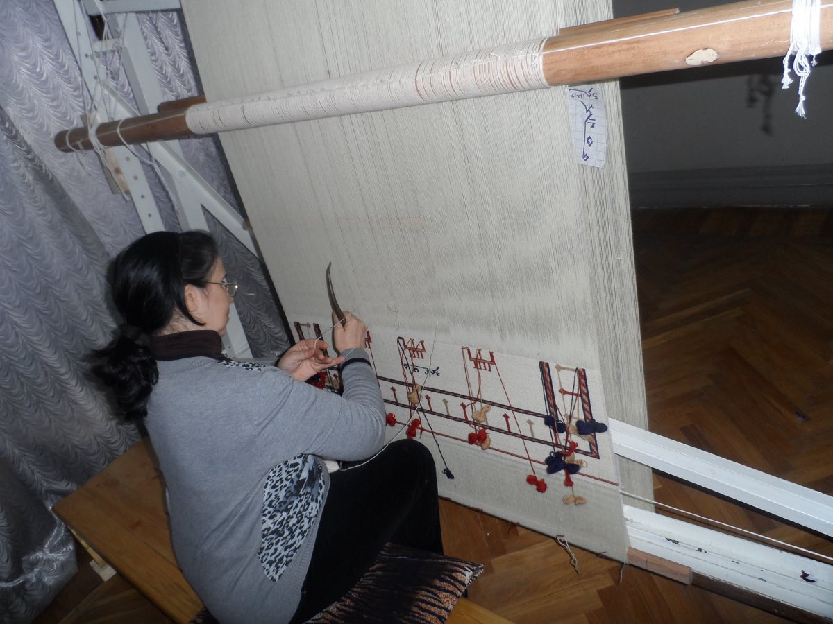 A weaver seated at an upright loom, weaving a kilim in Azerbaijan.