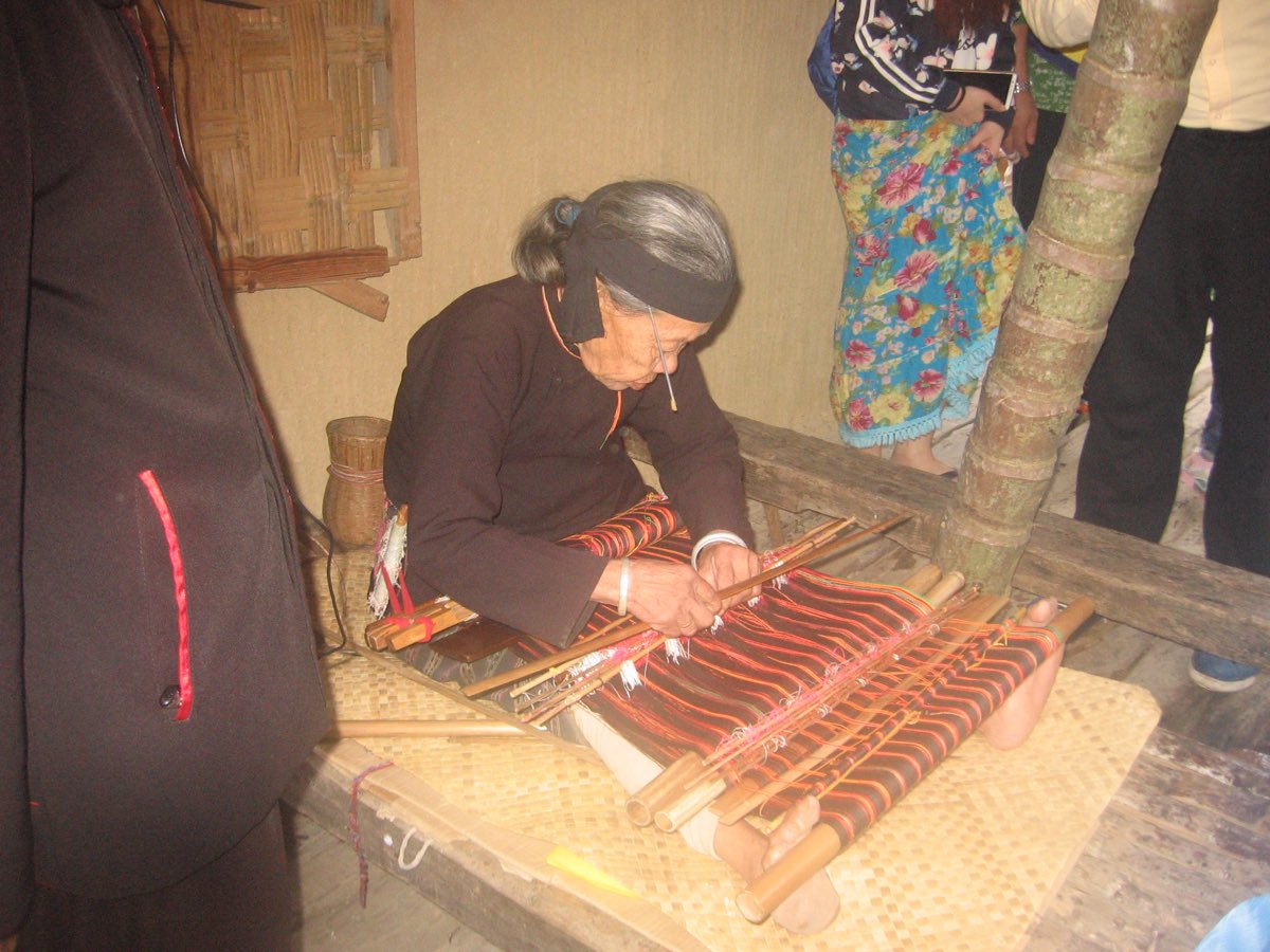 A Li weaver working red-patterned brocade on a foot-braced backstrap loom on Hainan island.