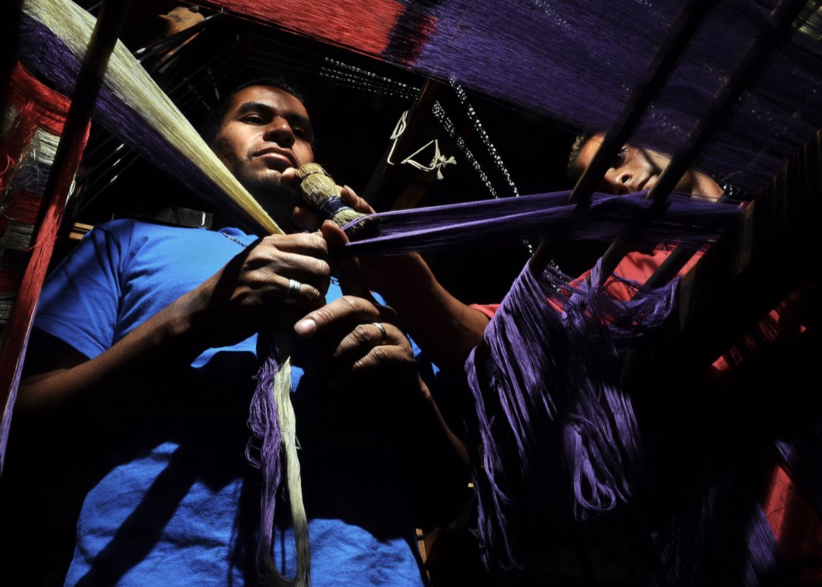 Young weavers in Tenancingo at the loom, handling deep-purple ikat warp threads for a rebozo.