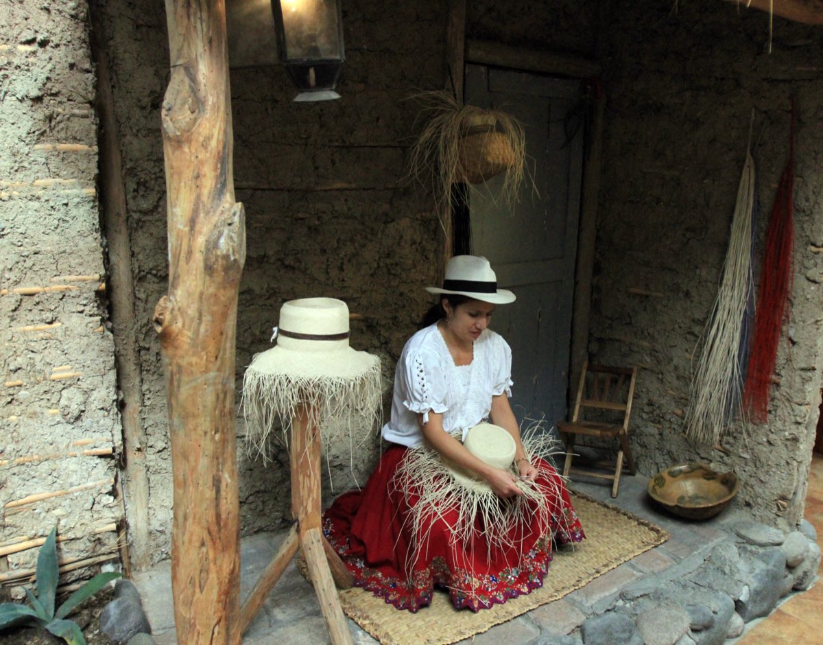 A weaver in Cuenca, Ecuador, hand-weaving a toquilla straw hat, loose straw fanning out around the unfinished crown.
