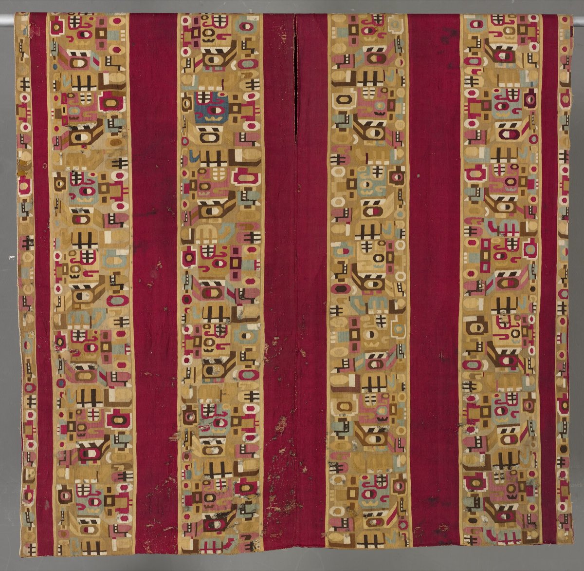 A Wari tapestry tunic, 7th–11th century — crimson bands alternating with columns of abstract figures.