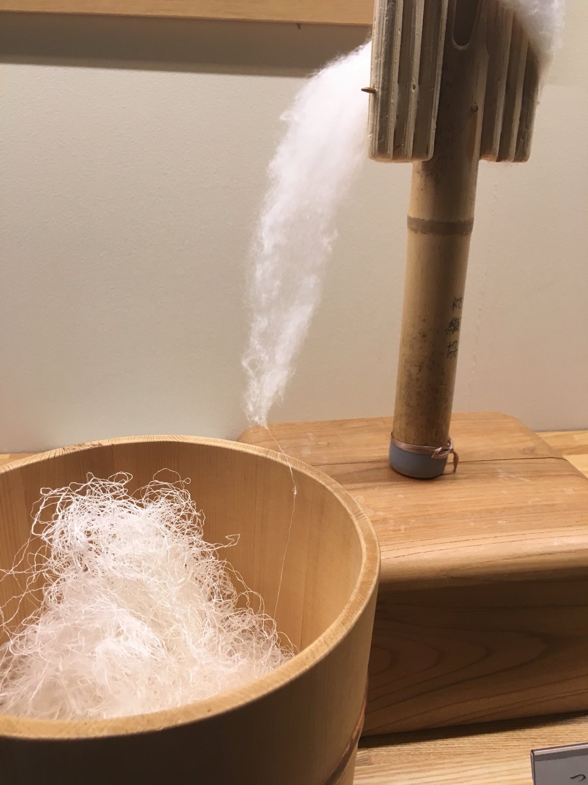 Floss silk mid-draw at a Yuki-tsumugi workshop — a cloud of mawata silk pulled down into a single untwisted thread.