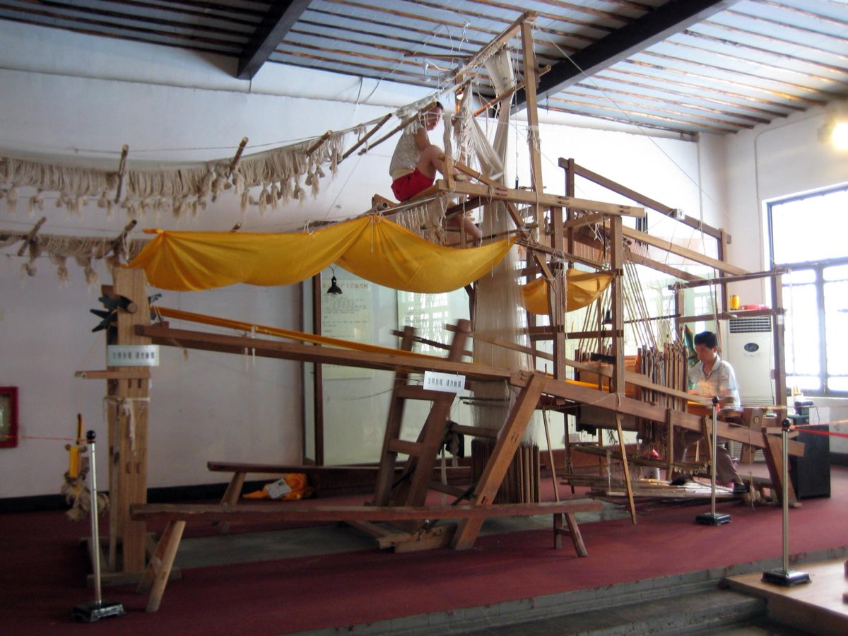 A two-person Yunjin drawloom in operation — one weaver perched on top working the pattern threads, one seated below.